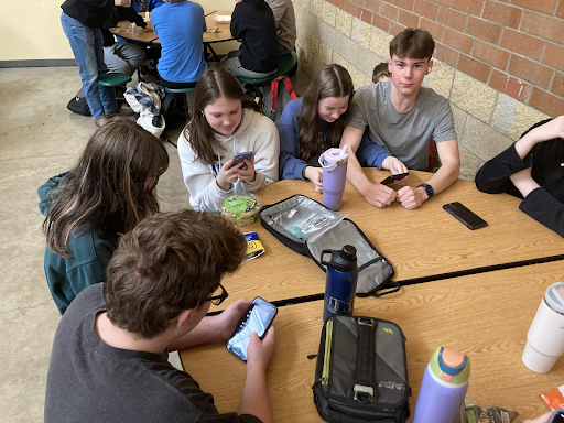Kids at a table in the commons during lunch use their phones on February 22, 2024